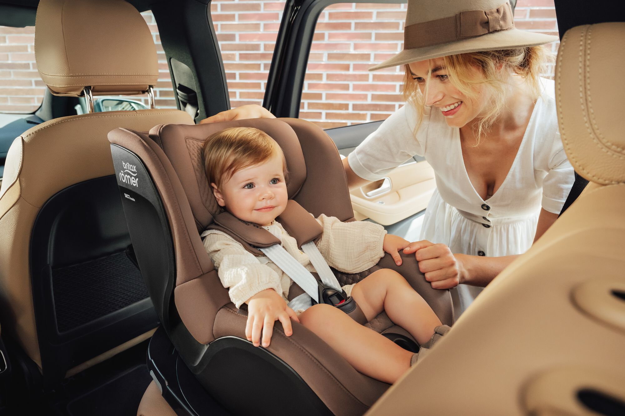 Tumling fastspændt i en DUALFIX 5Z toddler car seat, med sin mor stående ved siden af.